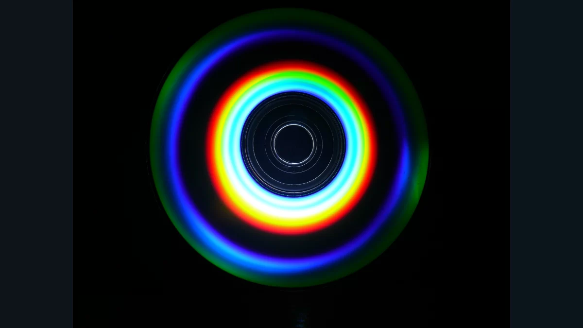 A compact disc reflecting circular bands of rainbow-coloured light against a dark background