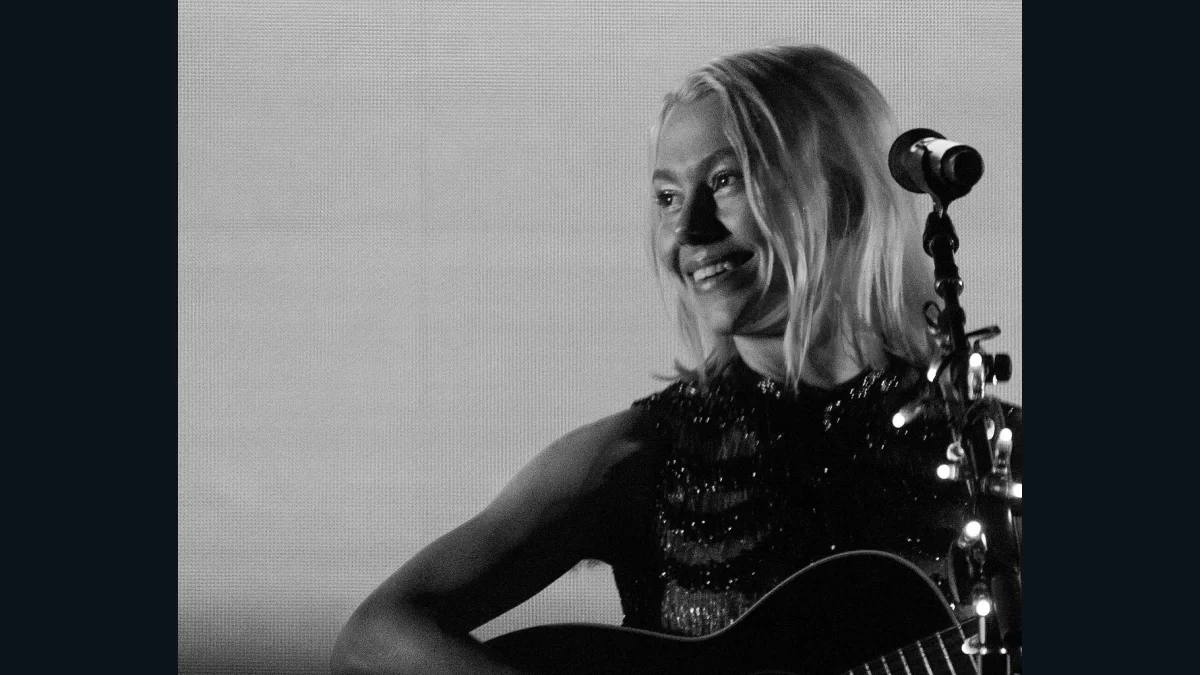 Phoebe Bridgers smiling beside a microphone with an acoustic guitar at Marymoor Park